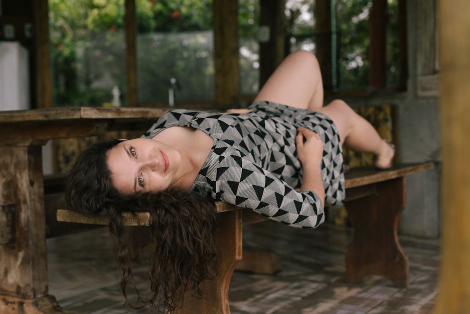 A woman in a patterned dress relaxes on a rustic wooden bench, capturing a moment of leisure.