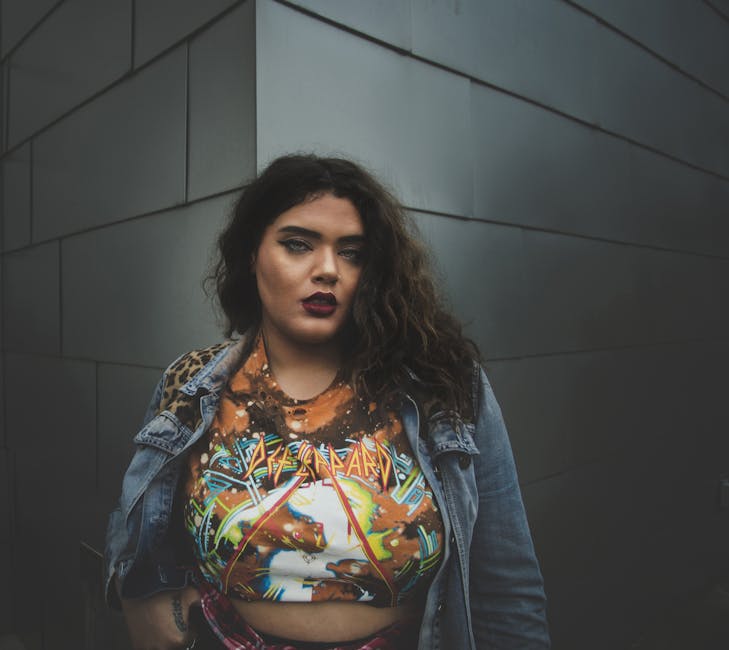 Confident young woman in fashionable attire posing outdoors against a sleek urban wall.