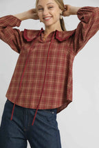 Woman wearing a red plaid shirt with ruffled collar on a gray background
